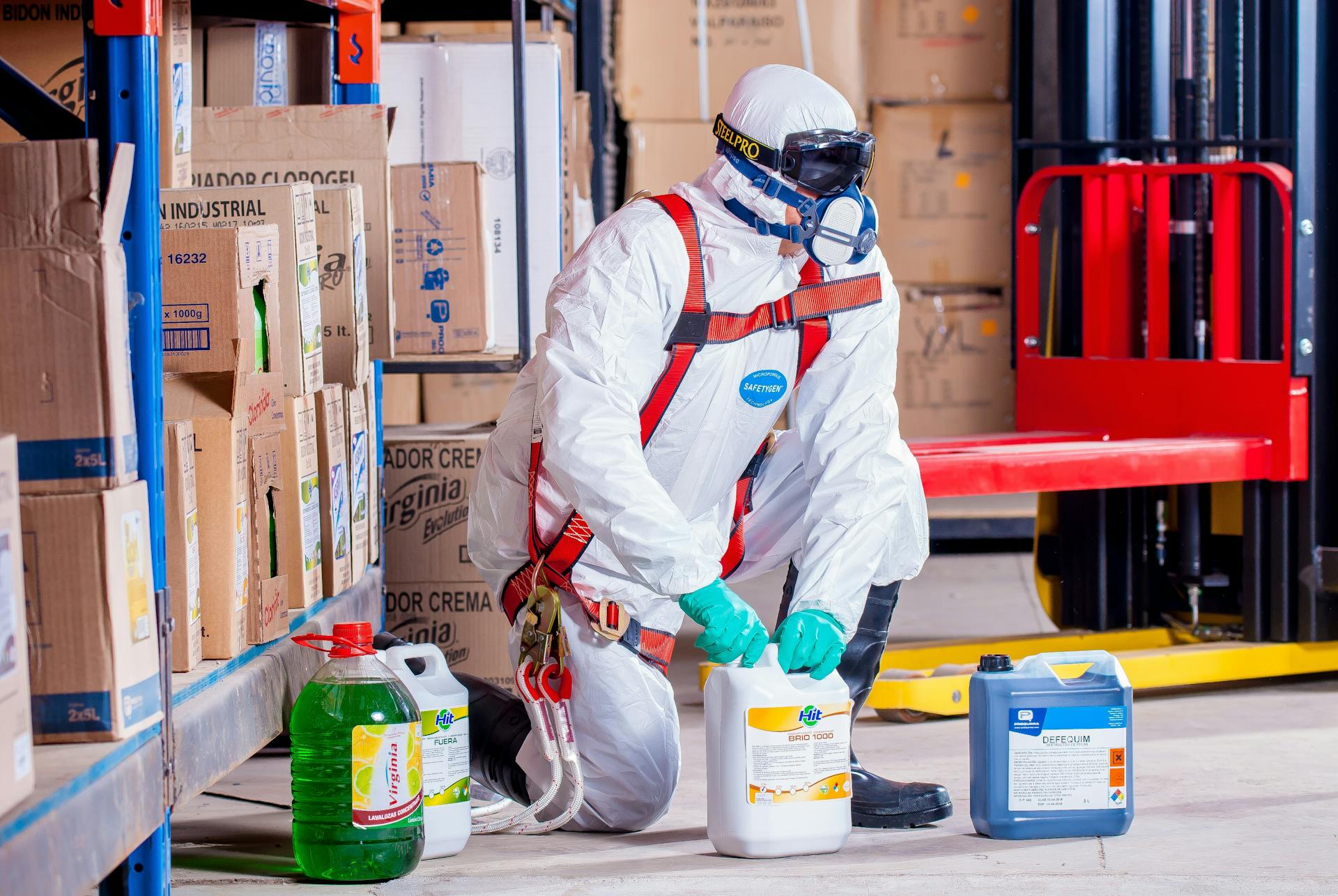 Worker in protective gear handling supplies among boxed items in a warehouse